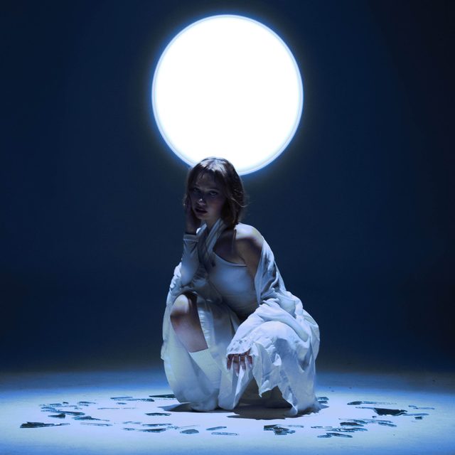 Cover art for I Killed Her by Djouher: the singer, dressed in white, crouches beneath a glowing full moon on a deep blue stage.